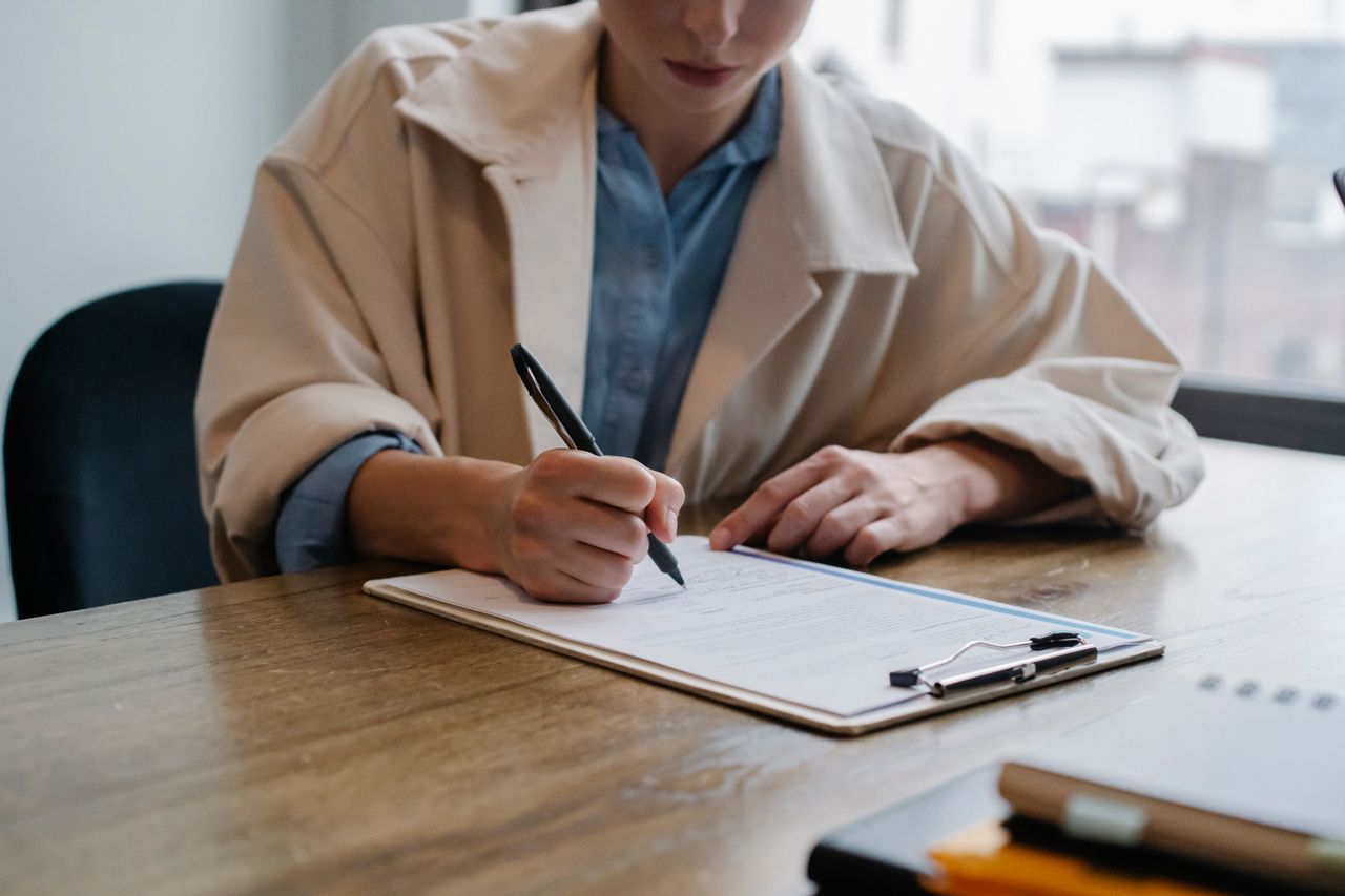 Crop young female unemployed job seeker filling questionnaire sitting at table during interview in office